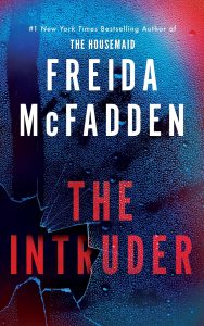 The Intruder by Freida McFadden — book cover with a dark cabin in the woods at night, a single lit window casting yellow light, storm clouds overhead.